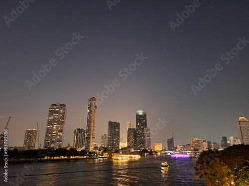 Nighttime scene of tall buildings adorned with lights by the riverside. Perfect for use as an illustration element or as a background