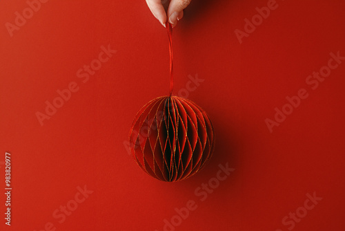 Happy holiday concepts, Hand holding Shining Christmas Ornaments of Red Paper, winter seasonal festive decorations as round ball on red fon, copy space, Creative trend Merry Christmas, New Year photo