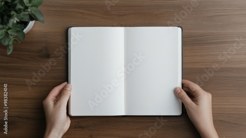 Hands holding an open blank notebook on a wooden table, ideal for writing, drawing, or planning ideas.