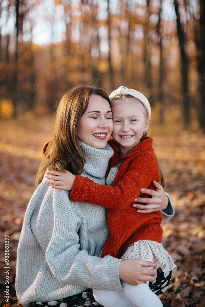 Mother is hugging her daughter with braids in an autumn forest. The woman, dressed in a gray sweater and skirt, is hugging her little daughter, who is wearing a red sweater, in the autumn forest. Mother is hugging her daughter with braids in an autumn forest. The woman, dressed in a gray sweater and skirt, is hugging her little daughter, who is wearing a red sweater, in the autumn forest.