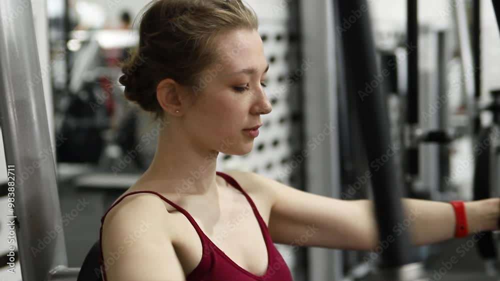 Young athletic pretty woman doing exercises on a chest machine in a fully equipped gym. Selective focus, camera movement. Young athletic pretty woman doing exercises on a chest machine in a fully equipped gym. Selective focus, camera movement.