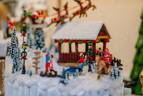 Oberammergau, Germany - September 14, 2024 - A miniature winter village scene with figurines, snow-covered trees, a sleigh, and festive decorations, capturing a cozy holiday atmosphere.. photo