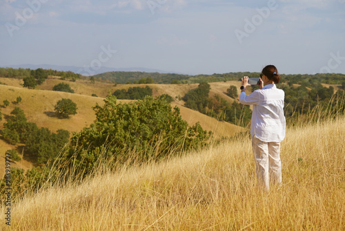 A charming girl enjoys the wind, smile and freedom, sunset and autumn light. Beautiful lady having fun in nature, she uses a smartphone and takes photos.