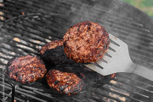 Idealnie wysmażony burger z mielonego mięsa wieprzowego, grillmaster przekręca kotlety na grillu  photo