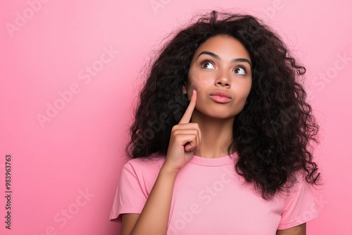 A woman with curly hair is looking up at the camera with a puzzled expression. She is wearing a pink shirt and she is deep in thought