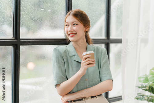 Coffee Break Confidence: A young woman enjoys a moment of calm with a cup of coffee, gazing out a window with a serene smile, radiating a sense of composure and quiet contentment. Free Download Coffee Break Confidence: A young woman enjoys a moment of calm with a cup of coffee, gazing out a window with a serene smile, radiating a sense of composure and quiet contentment. - GFXLoad