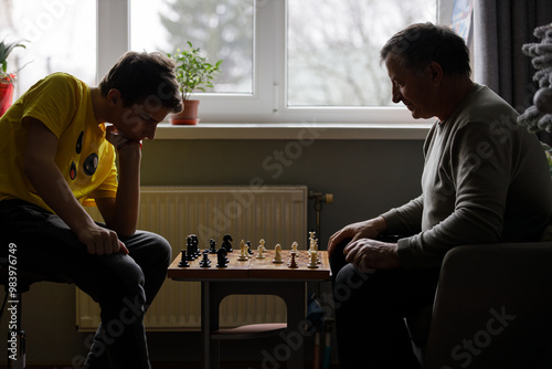 Young boy playing chess with his grandfather indoors during a quiet afternoon