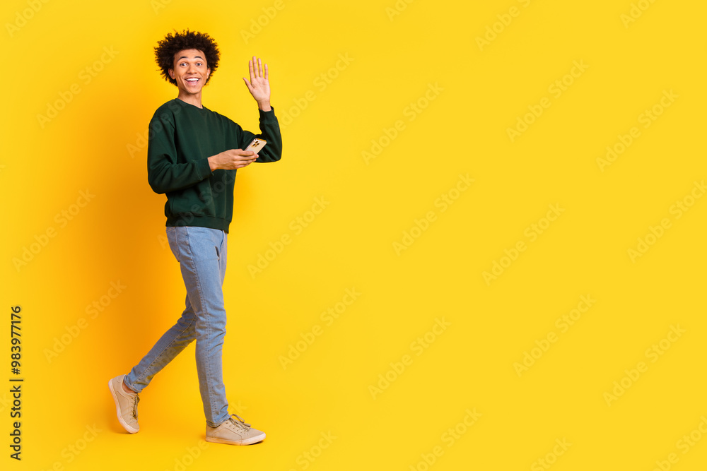 Full size photo of nice young man walk phone arm wave wear pullover isolated on yellow color background Full size photo of nice young man walk phone arm wave wear pullover isolated on yellow color background