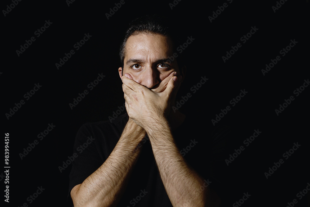 Man covering his mouth with his hand. Low key male portrait.