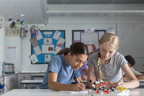 Two girl students in science class working on a project with a molecular model together