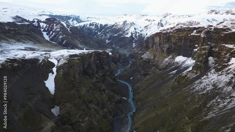 Drone shot of a deep canyon with snow-capped cliffs and a winding river in Búrfell, Iceland, surrounded by rugged mountains and dramatic terrain. Drone shot of a deep canyon with snow-capped cliffs and a winding river in Búrfell, Iceland, surrounded by rugged mountains and dramatic terrain.