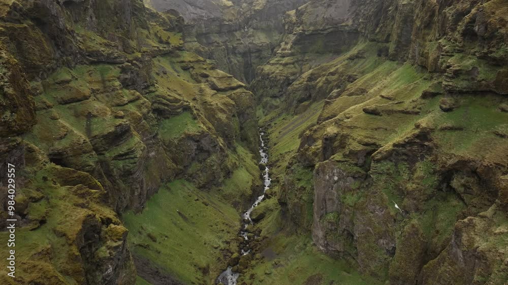 Aerial shot of a narrow river flowing through a steep, moss-covered canyon in Brókarjökull, Iceland, surrounded by towering cliffs and rugged terrain. Aerial shot of a narrow river flowing through a steep, moss-covered canyon in Brókarjökull, Iceland, surrounded by towering cliffs and rugged terrain.