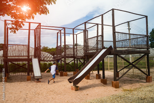 Children playground on sand yard activities in public park surrounded by green trees at sunlight morning. built climbing slide, seesaw on vintage playground.  photo