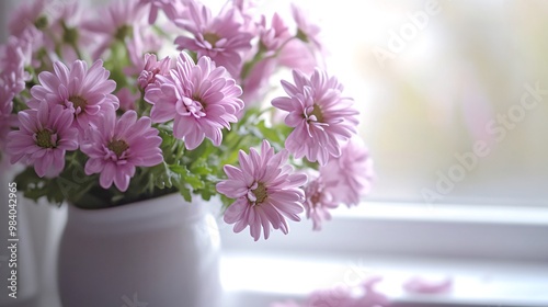 A vase of pink flowers sits on a windowsill with a blurred background.