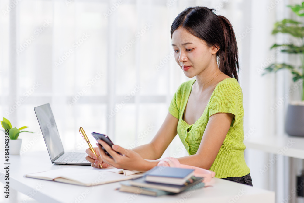 Asian employer using smartphone and taking notes on laptop while working in the home office, Free Space Asian employer using smartphone and taking notes on laptop while working in the home office, Free Space