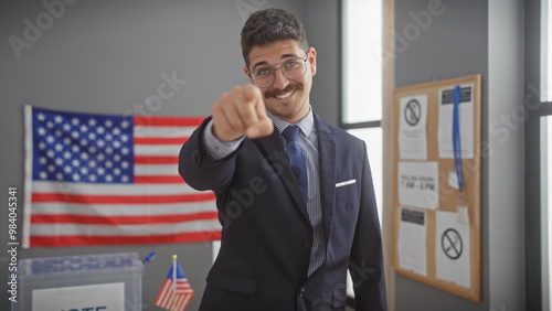 Hispanic man in suit pointing at camera in us voting center with american flag. photo