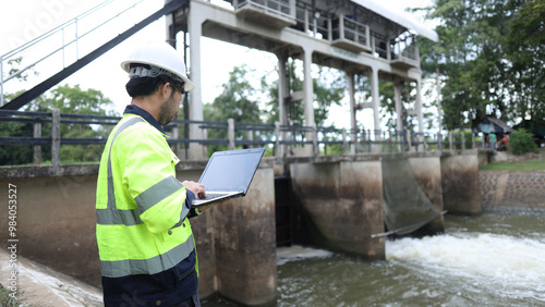 Portrait of engineer wearing green vest and white helmet with tablet Working day on a water dam with a hydroelectric power plant. Renewable energy systems, Sustainable energy concept