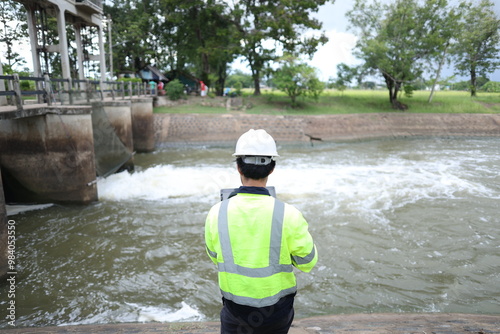 Portrait of engineer wearing green vest and white helmet with tablet Working day on a water dam with a hydroelectric power plant. Renewable energy systems, Sustainable energy concept