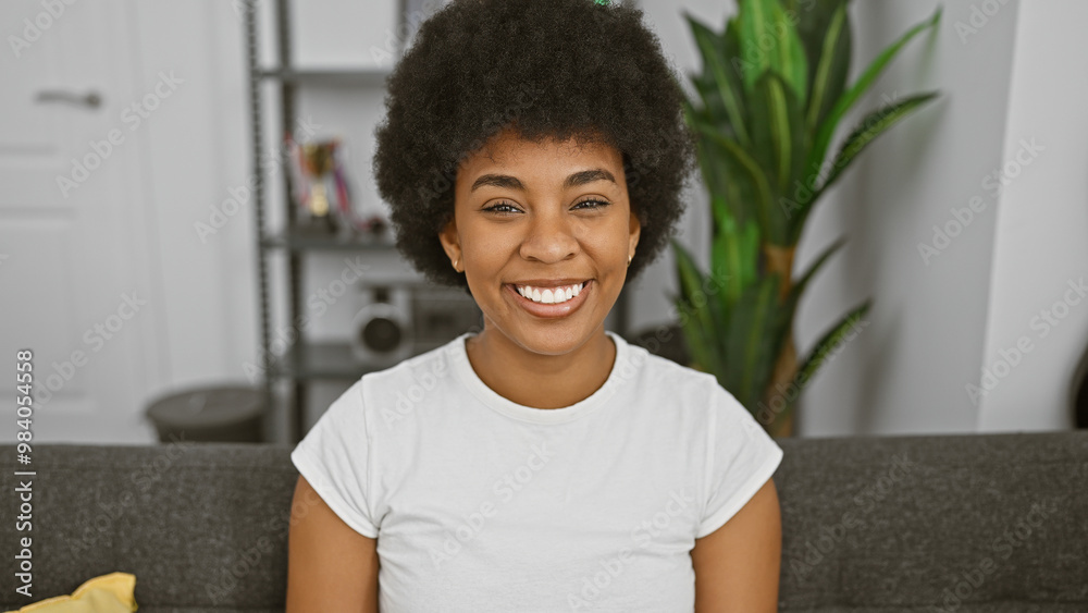 Fototapeta premium Beautiful african american woman with curly hair smiling in her cozy living room.