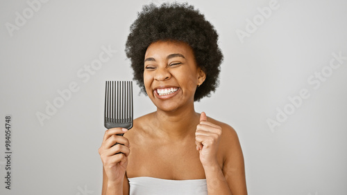 Foto A joyful african american woman with curly hair holds a comb against a white background, exuding beauty and positivity