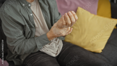 A young hispanic man experiences wrist pain while sitting on a couch indoors, creating a personal healthcare theme.