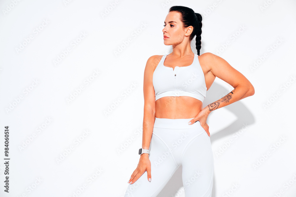 Portrait of fitness confident woman in white sports clothing. Sexy young beautiful model with perfect body. Female isolated on white wall in studio. Stretching out before training Portrait of fitness confident woman in white sports clothing. Sexy young beautiful model with perfect body. Female isolated on white wall in studio. Stretching out before training
