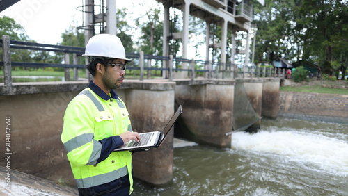Portrait of engineer wearing green vest and white helmet with tablet Working day on a water dam with a hydroelectric power plant. Renewable energy systems, Sustainable energy concept