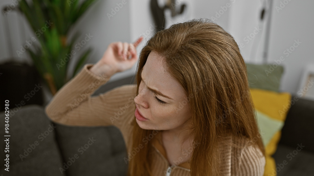 Fototapeta premium A contemplative young blonde woman in a casual sweater indoors, seated in a modern living room.