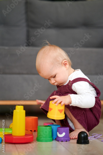 Adorable cute beautiful little baby girl playing with educational toys at home or nursery. Happy healthy child having fun with colorful wooden rainboy toy pyramid.