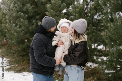 Parents and little child in a pine forest in winter. 