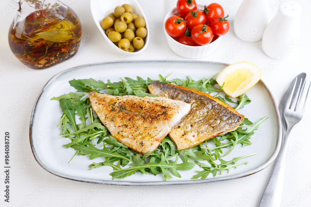 Fried dorado fillet with crispy skin. Arugula, cherry tomatoes, olives, lemon and olive oil. Traditional Mediterranean dish. White background. Selective focus, close-up. Fried dorado fillet with crispy skin. Arugula, cherry tomatoes, olives, lemon and olive oil. Traditional Mediterranean dish. White background. Selective focus, close-up.