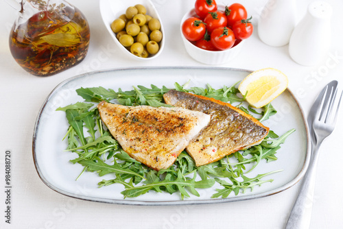 Fried dorado fillet with crispy skin. Arugula, cherry tomatoes, olives, lemon and olive oil. Traditional Mediterranean dish. White background. Selective focus, close-up.