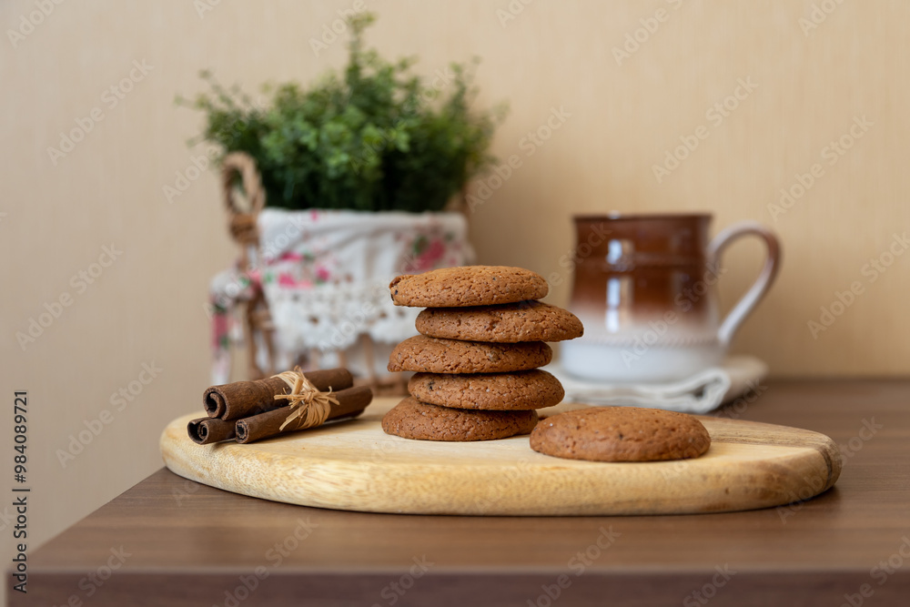 Oatmeal raisin cookies on a wooden board with cinnamon (cassia) sticks and a cup of milk. Traditional homemade pastry in rustic style. Selective focus, close-up. Oatmeal raisin cookies on a wooden board with cinnamon (cassia) sticks and a cup of milk. Traditional homemade pastry in rustic style. Selective focus, close-up.