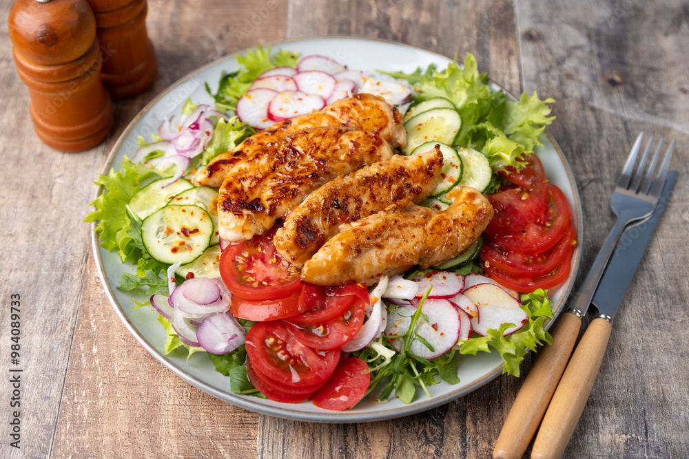 Warm salad with baked chicken breast and fresh vegetables, dressed with olive oil on a wooden background. Home kitchen in rustic style. Hearty delicious food. Selective focus, close-up. Warm salad with baked chicken breast and fresh vegetables, dressed with olive oil on a wooden background. Home kitchen in rustic style. Hearty delicious food. Selective focus, close-up.