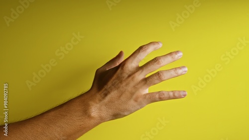 Man's hand reaching out with fingers spread against a bright yellow background, highlighting texture and color contrast.