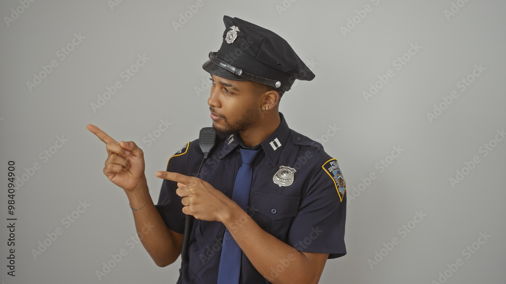 A confident black police officer pointing sideways against a white background, portraying authority and guidance. A confident black police officer pointing sideways against a white background, portraying authority and guidance.