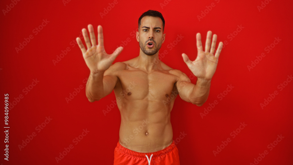 Fototapeta premium Young hispanic man making a stop gesture with his hands over an isolated red background, exuding confidence and determination.