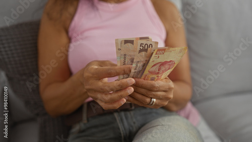 Woman counting mexican pesos while sitting in her living room, highlighting casual domestic environment and focus on hands and money