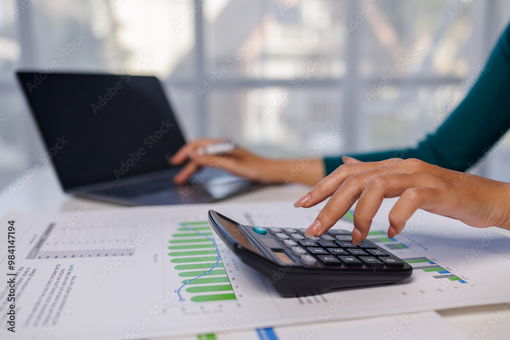 Close up of female hand accountan using a laptop computer and calculator to calculate taxes at desk in the office financial business, calculating accounting online marketing. Close up of female hand accountan using a laptop computer and calculator to calculate taxes at desk in the office financial business, calculating accounting online marketing.