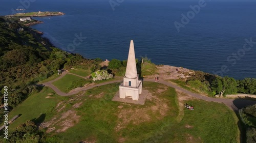 Killiney Hill, County Dublin, Ireland, June 2023. Drone slowly orbits The Obelisk clockwise revealing the view south towards Killiney Bay, Bray and the Wicklow Mountains on a bright sunny afternoon. photo