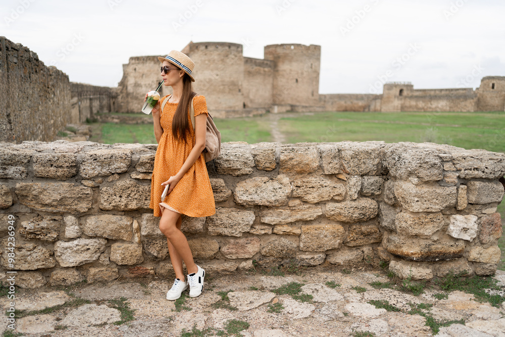 Fototapeta premium Tourist in ancient fortress drinks cocktail near castle at sunset