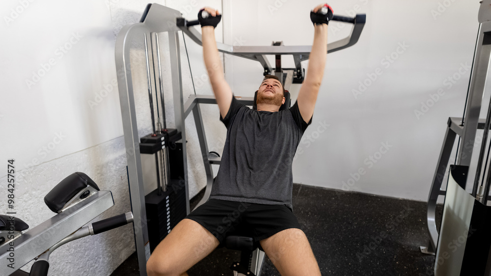Fototapeta premium A Caucasian man exercises on a chest press machine in a gym, emphasizing fitness and health during New Year's resolutions