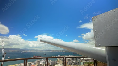 A historic cannon overlooking the city of Gibraltar, with a wide view of the bay and mountains in the distance under a clear blue sky