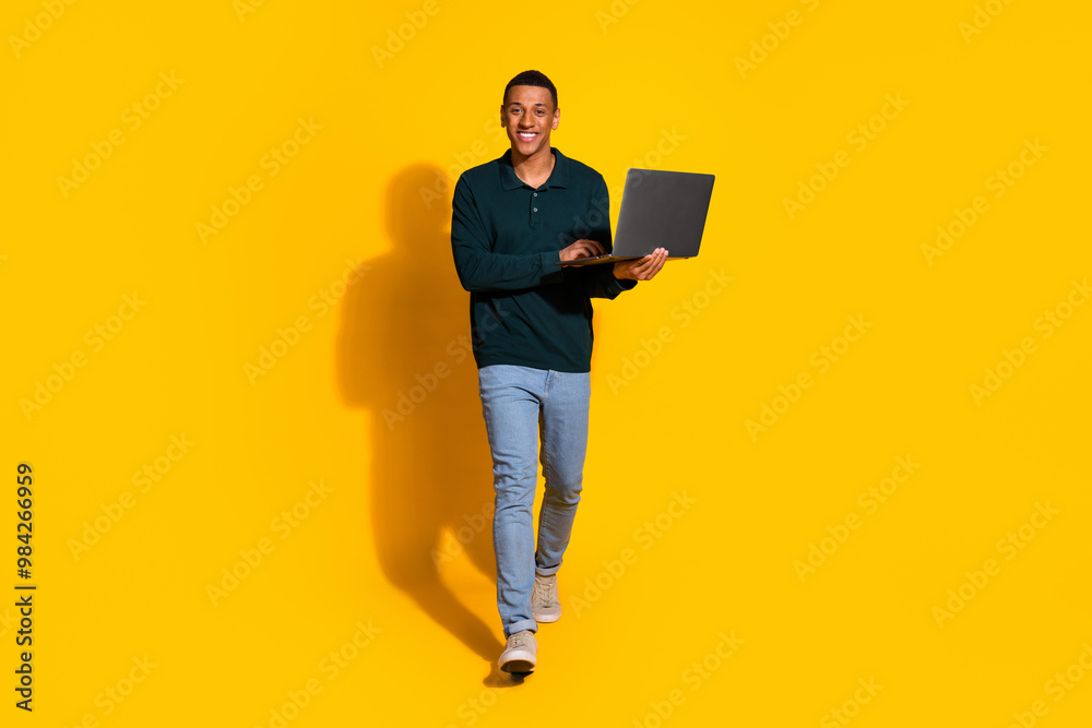 Full length photo of attractive young man going hold netbook dressed stylish green clothes isolated on yellow color background Full length photo of attractive young man going hold netbook dressed stylish green clothes isolated on yellow color background