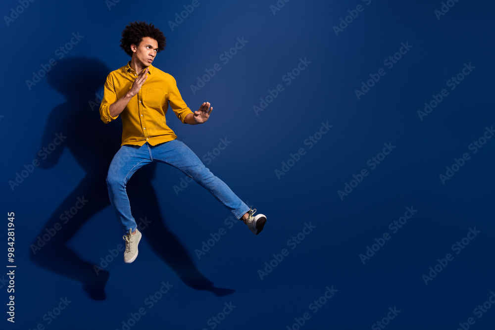 Fototapeta premium Full body portrait of nice young man jump fight empty space wear yellow shirt isolated on dark blue color background