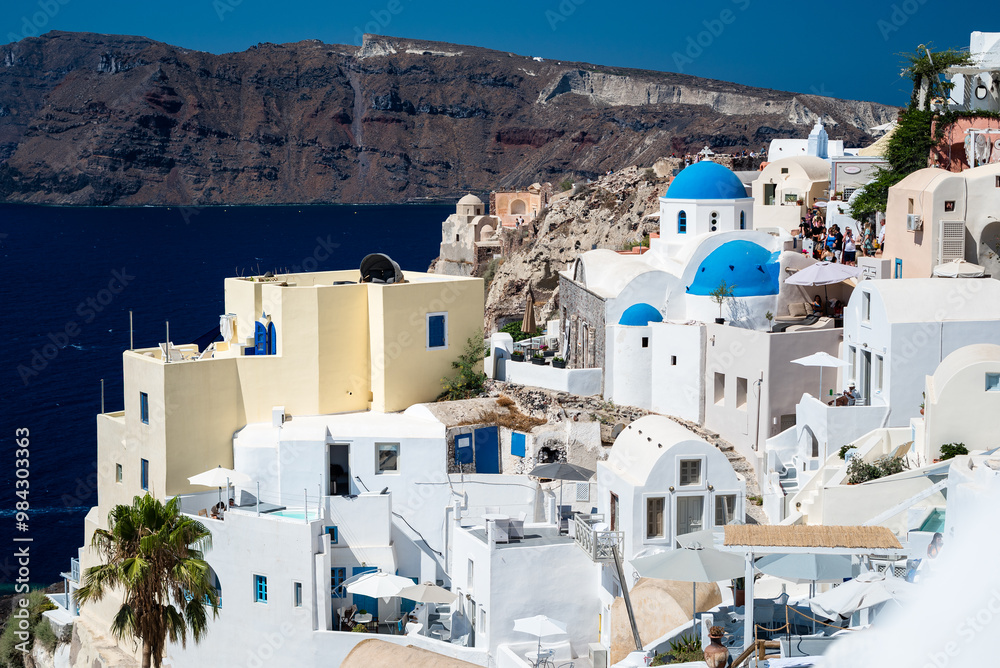 Views of Santorini. Stunning hillside covered with whitewashed houses, some adorned with iconic blue domes, cascading down towards sea. Traditional Cycladic architecture Views of Santorini. Stunning hillside covered with whitewashed houses, some adorned with iconic blue domes, cascading down towards sea. Traditional Cycladic architecture