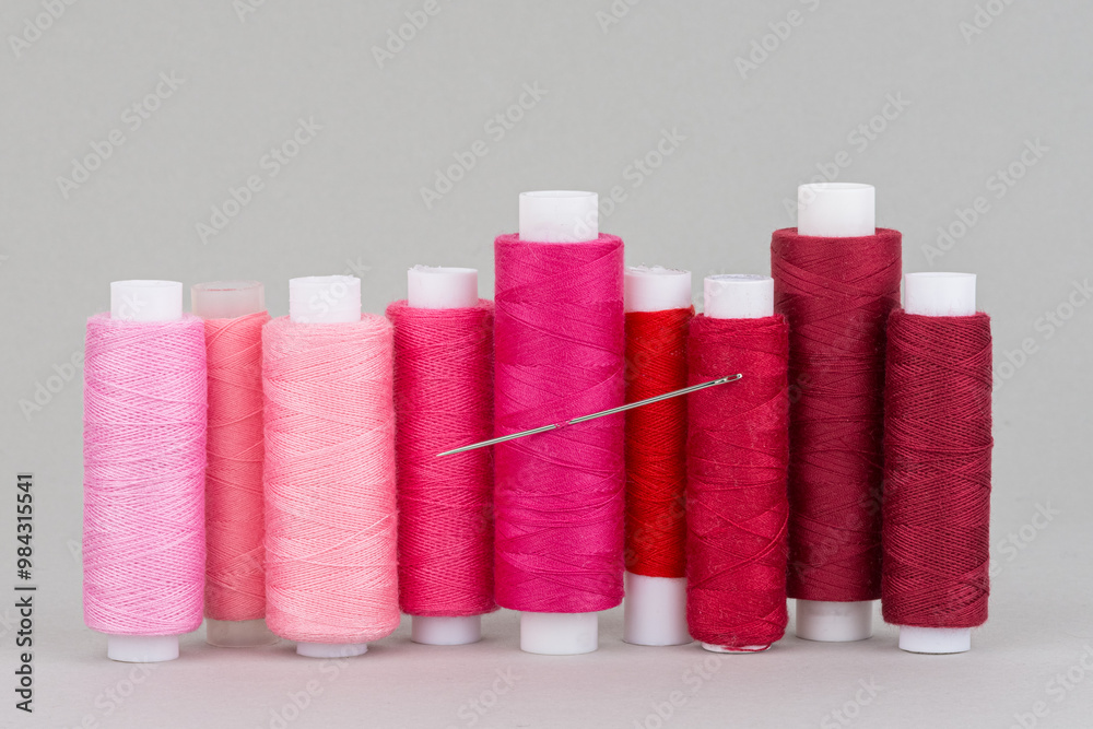Red and pink thread spools with needle on grey background Red and pink thread spools with needle on grey background