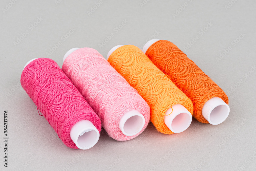 Red orange pink thread spools on grey background. Red orange pink thread spools on grey background.