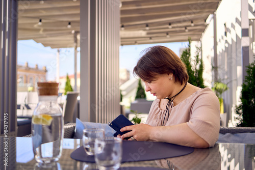 Free Download plus size woman in peach fuzz dress chooses a dish in a restaurant via QR code in smartphone, water with lemon and glasses in front of her - GFXLoad