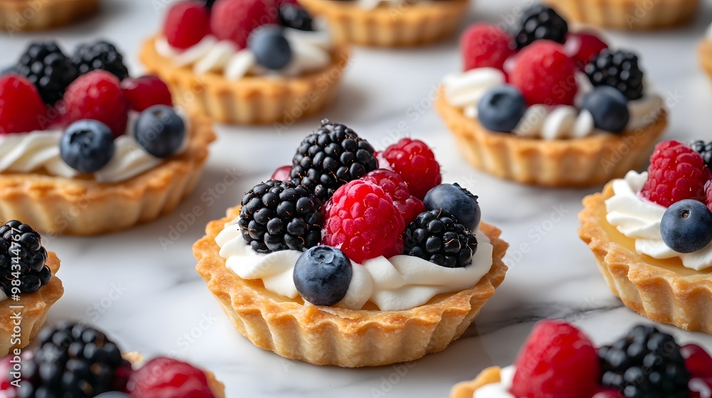 Mini fruit tarts with fresh berries topping, including raspberries, blackberries, and blueberries, on a white marble tabletop with shallow depth of field and elegant presentation. Mini fruit tarts with fresh berries topping, including raspberries, blackberries, and blueberries, on a white marble tabletop with shallow depth of field and elegant presentation.
